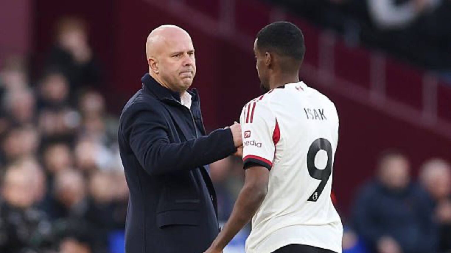 Alexander Isak shaking hands with his manager Arne Slot on the pitch in a Liverpool kit.