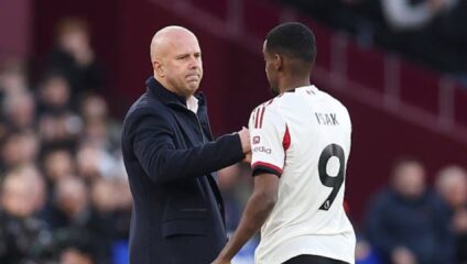Alexander Isak shaking hands with his manager Arne Slot on the pitch in a Liverpool kit.