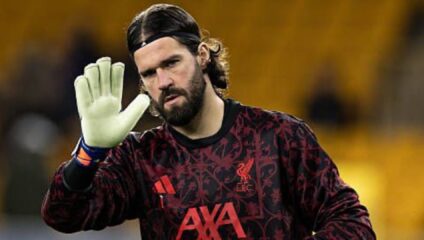 Alisson Becker in a Liverpool goalkeeper kit, waving.